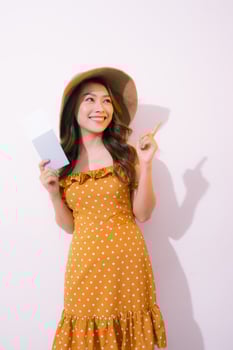 Cheerful young woman standing isolated over pink background, showing passport with flight tickets photo