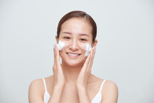 Portrait of young Asian woman applying foaming cleanser against white background. photo