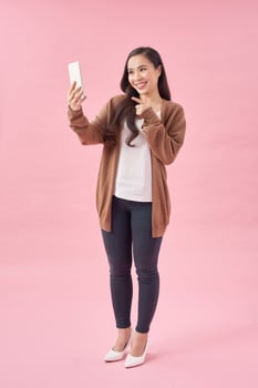 Happy young asian woman casually dressed standing isolated over pink background, using mobile phone photo