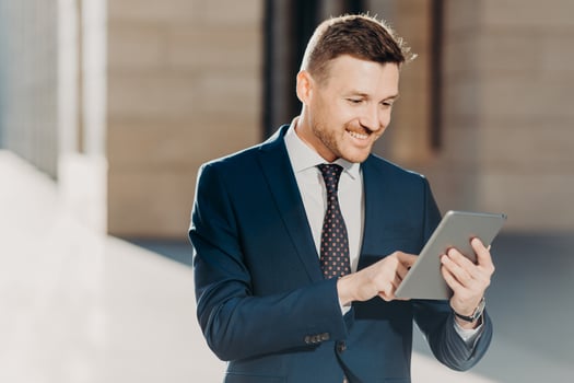 Succesful male entrepreneur in formal suit, holds modern tablet, checks documentation online, reads necessary information for making business report, uses free wifi connection. People and technology photo