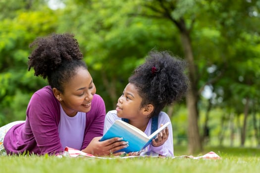 African American mother is teaching her young daughter to read while lying down after having a summer picnic in the public park for education and happiness concept photo