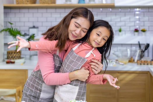 Happy Asian mother is hugging her daughter while having fun time after cooking in the kitchen for love and family concept photo