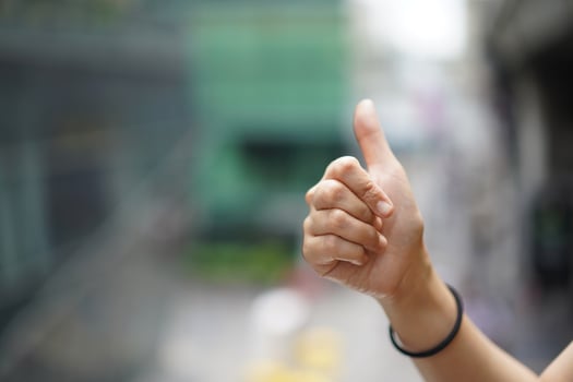 Women raise up the thumb with blur green background near sky train, Bangkok, Thailand. photo