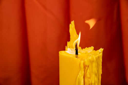 Close up to the melt yellow candle and fire flame with the red curtain background. photo