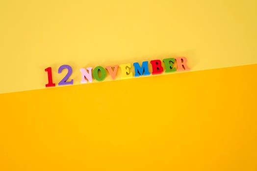 November 12 on a yellow, paper background with wooden and multicolored letters with space for text. photo