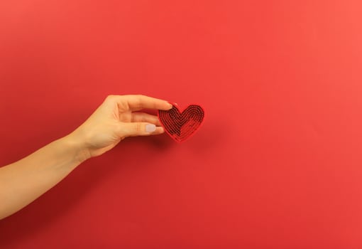 A womans hand holds a red heart on a red background photo