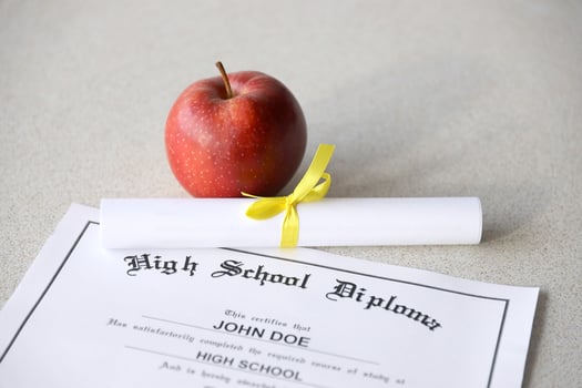 A high school diploma lies on table with small scroll and red apple. Education documents photo