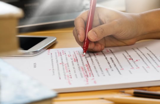 hand holding red pen over proofreading text photo