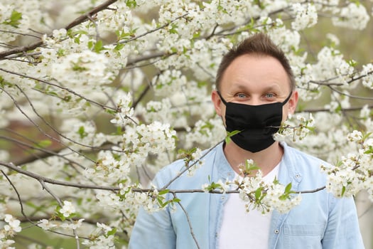 man in mask among flowering trees. man in a medical mask among a blossoming spring garden. Self-isolation and quarantine. cheerful man rejoices in the end of the pandemic and enjoys the spring. photo