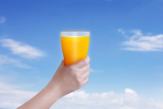 Female hand holding a glass of orange juice against a bright sky background. photo