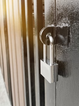Silver padlock closed and locked hang on hole steel fence gate door of home with orange light evening close-up. photo