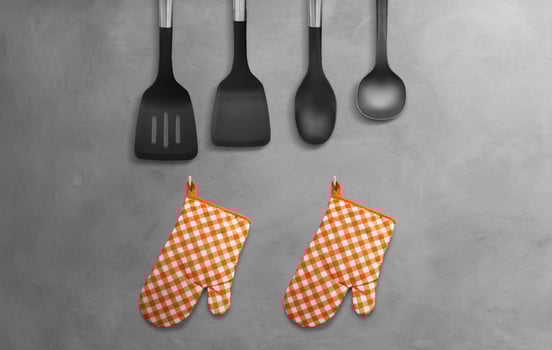 Orange heat resistant cooking gloves with kitchen utensils hanging on cement wall. photo