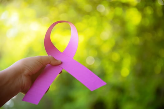 Pink paper ribbon holding in hands of female teenager to show and to call out all people around the world to support and to attend the breast cancer campaign of woman, soft and selective focus. photo