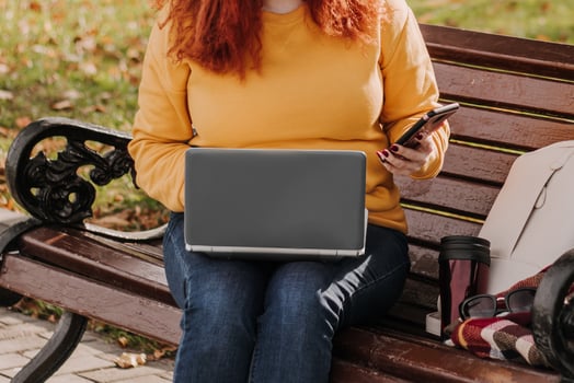 Young red-haired woman freelancer works in park using laptop. Modern businesswoman talking on phone. Online work on Internet. photo