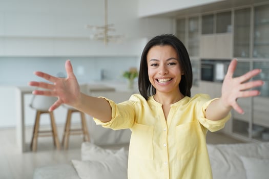 Smiling woman stretches arms to hug, looking at camera, meeting guests, giving warm welcome at home photo