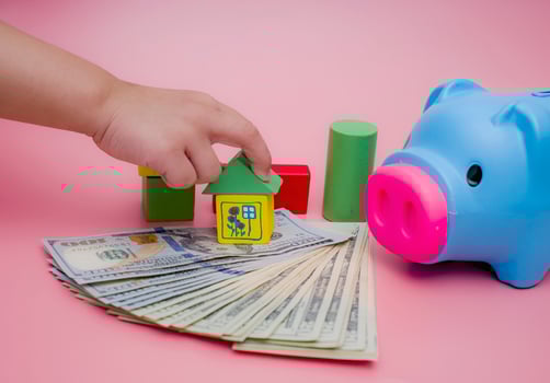 Hand of the kids take a wood block with small  house models on top of block.Concept of saving money for future , investment property and saving money to buy a house. On blur background. photo