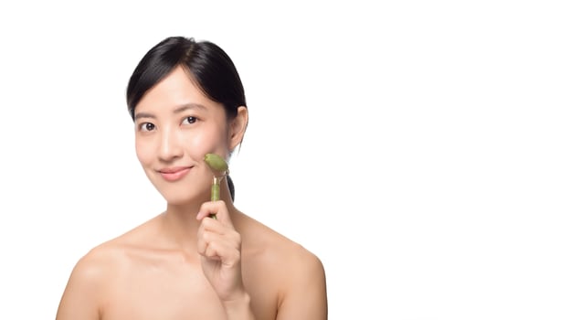 Studio shot of an attractive young asian woman using a jade roller on her face against a white background. photo