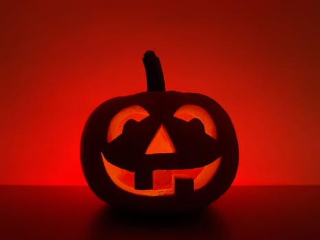 Halloween holiday background with traditional smiling jack-o-lantern. Big carved glowing pumpkin stands on the surface in dark night. The back wall highlighted in red. photo