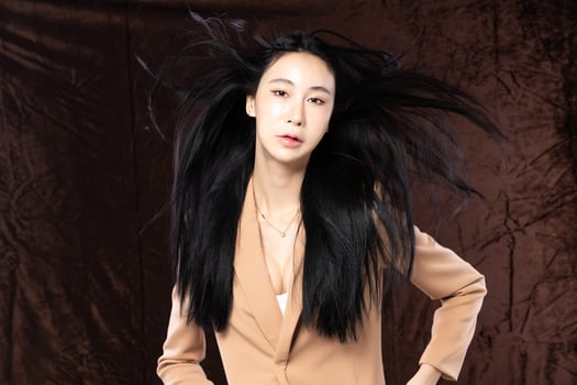 Haft body portrait of beautiful transgender 20s asian woman express feeling smiling confidently on brown background. Business Female smart look blazer has wind blow throw her hair in air, copy space photo