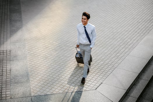 Happy Young Businessman Walking with Suitcase in the City. Modern Male in Business Trip. High Angle View. Full Length photo