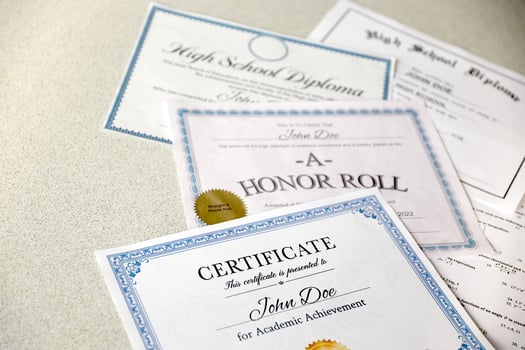 A honor roll recognition, certificate of achievement and high school diploma lies on table. Education documents photo