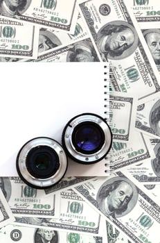 Two photographic lenses and white notebook lie on the background of a lot of dollar bills. Space for text photo