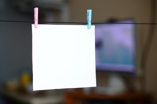White blank card on rope, dark office background. Creative reminder, small sheet of paper on wooden clothespin, memo backdrop photo