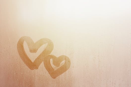 Couple of abstract blurred love heart symbol drawn by hand on the wet window glass with sunlight background. Template for Valentine Day postcards photo