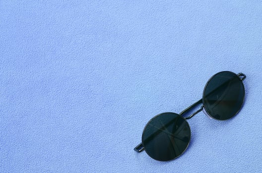Stylish black sunglasses with round glasses lies on a blanket made of soft and fluffy light blue fleece fabric. Fashionable background picture in female colors photo