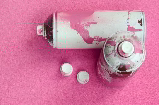 Some used pink aerosol spray cans and nozzles with paint drips lies on a blanket of soft and furry light pink fleece fabric. Classic female design color. Graffiti hooliganism concept photo