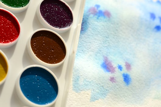 A new set of watercolors lies on a sheet of paper, which shows an abstract watercolor drawing in the form of blue strokes. The concept of amateur painting among teenagers photo