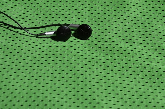 Black earphones lie on the green sportswear of polyester nylon fiber. The concept of listening to music during sports training with modern technology photo