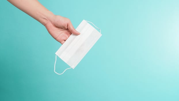 Hand is holding white medical face mask on mint green background. photo
