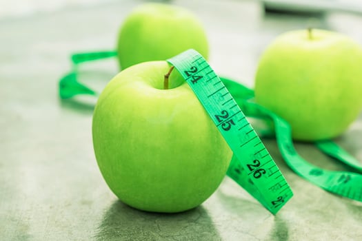 Measure tape and green apple on stone background. photo