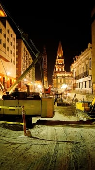 Construction at night, heavy machinery, backhoe, grader, road roller, a church in the background photo