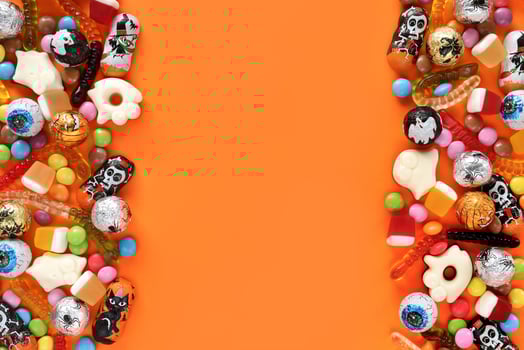 Halloweem orange background with copy space in middle, assorted candies on both sides - traditional eyeballs chocolates, jelly worms, ghosts. Happy Halloween holiday sale and trick-or-treat concept. photo