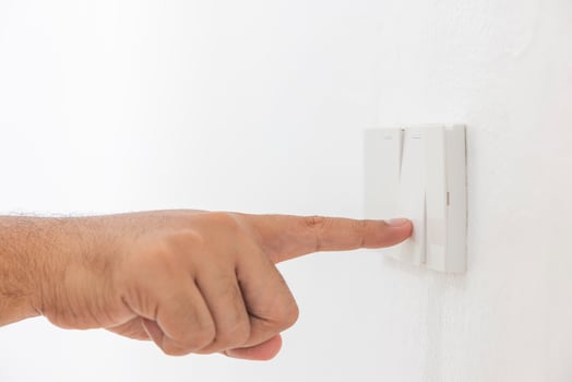 Close-up light switch of a male finger will turn on or off a light switch with white wall at home. white plastic mechanical switch mounted. Energy, energy, save electricity, copy space photo