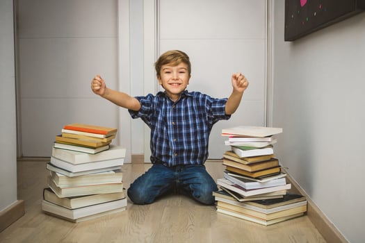 Excited kid with hands raised with books around him. photo