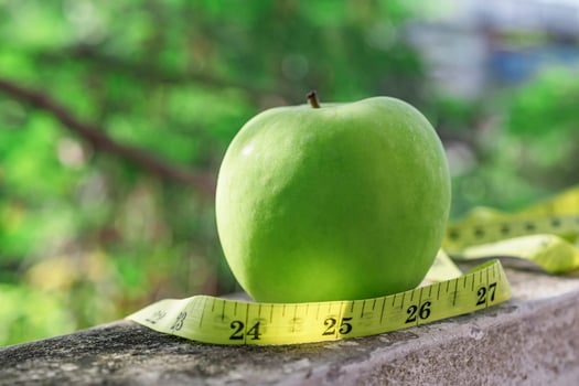 Measure tape and green apple on stone background. photo