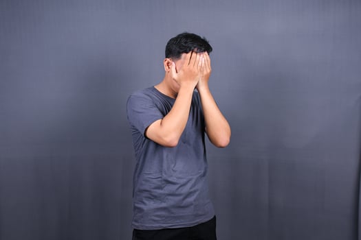Depressed Asian Young man having stressful time with hands covering face. isolated on gray background. photo