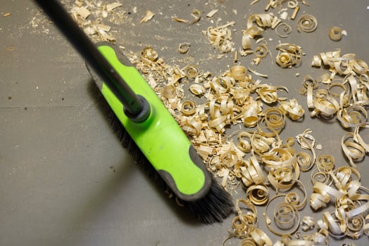 a small pile of wood shavings on a gray linoleum floor with a broom brush photo