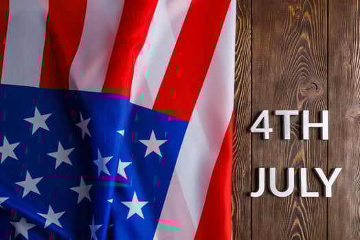 the words 4th july and crumpled usa flag on flat textured wooden surface background photo