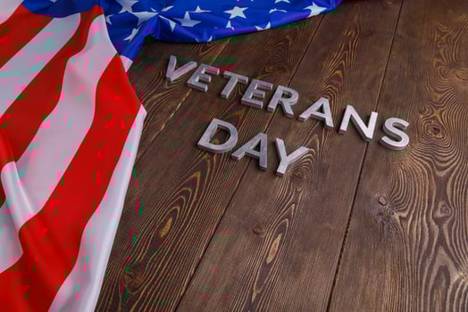 the words veterans day laid with silver metal letters on wooden board surface with crumpled usa flag photo