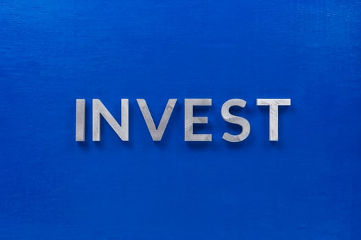 the word invest laid with silver metal characters on blue painted wooden board in central flat lay composition photo