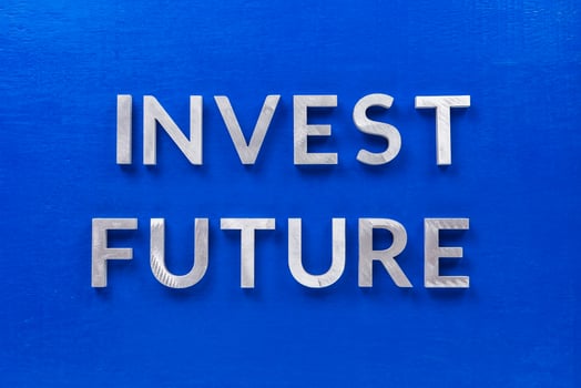 the words invest future laid with silver metal characters on blue painted wooden board in central flat lay composition photo