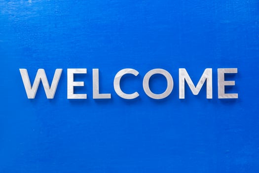the word welcome laid with silver metal characters on blue painted wooden board in flat lay with central composition photo