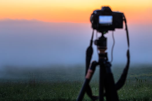 black digital camera on tripod shooting foggy morning landscape at summer with selective focus photo