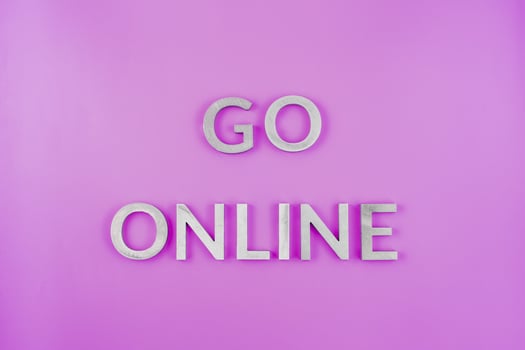 the words go online laid with brushed aluminium letters on flat pink surface - close-up with flat lay composition photo