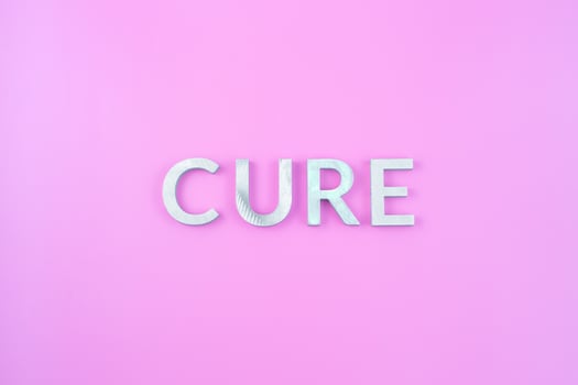 the word cure laid with thick aluminium letters on pink background photo