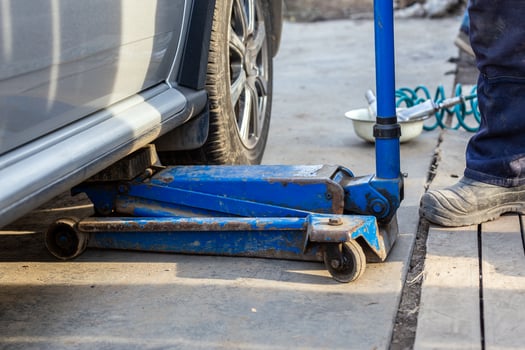 Silver civil car lifting with old hydraulic floor jack in a outdoor car workshop. Season tire changing procedure. photo